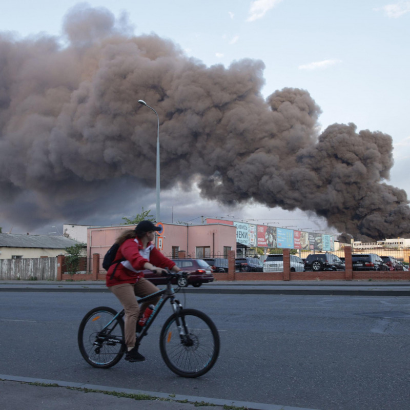 Una donna in sella a una bicicletta supera una nuvola di fumo di un incendio sullo sfondo dopo un attacco missilistico a Odessa