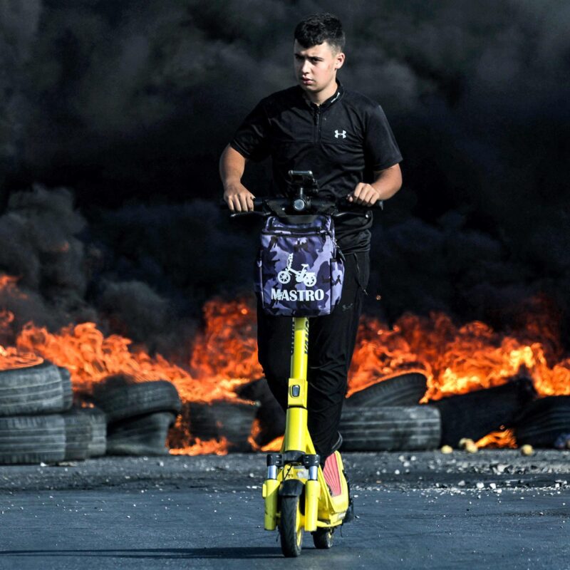 Un manifestante palestinese guida uno scooter davanti a pneumatici in fiamme durante gli scontri con i soldati israeliani nella città di Ramallah, nella Cisgiordania
